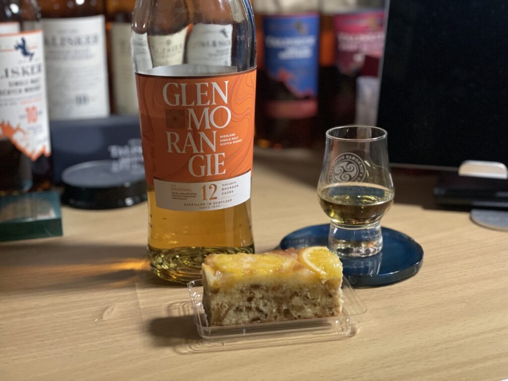 テーブルに置かれたグレンモーレンジィ12年のボトルとテイスティンググラス、そしてオレンジケーキの写真