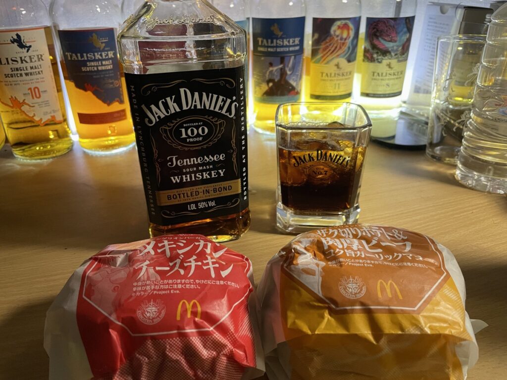 テーブルに置かれたジャックダニエルボトルドインボンドのボトルとマクドナルドのハンバーガーの写真