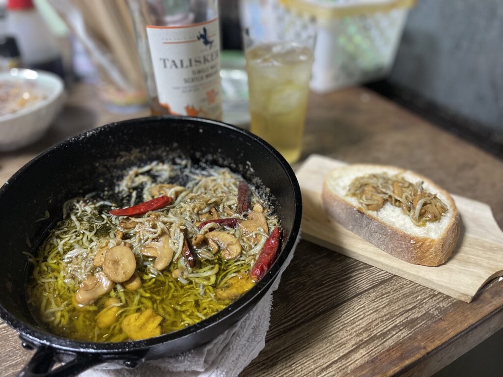 テーブルに置かれたスキレットで作られたちりめんアヒージョとそれを乗せて食べるバゲットの写真